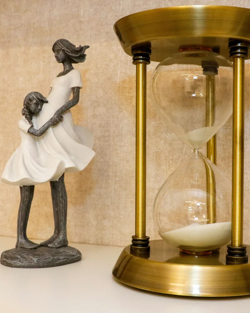 Escultura de mãe e filha ao lado de uma ampulheta, na estante do consultório